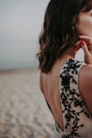 A tanned brunette stands in a dress with an open back. Beautiful lines bends the back. Refined sensual details of a female on the background of the seaの写真素材