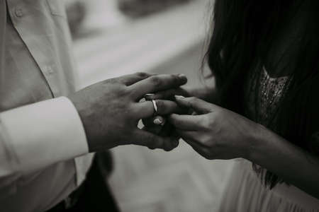 The bride and groom exchange wedding rings. Hands from a close distance. Black and white background.