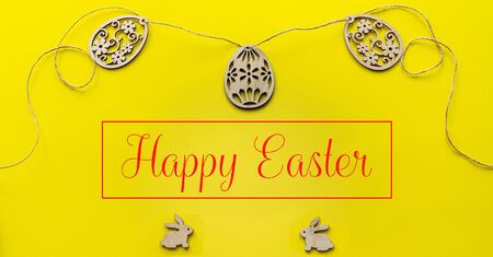 Flatlay with wooden figured eggs connected by twine and with two toy rabbits on a yellow paper background. Top view of easter concept with text.の写真素材