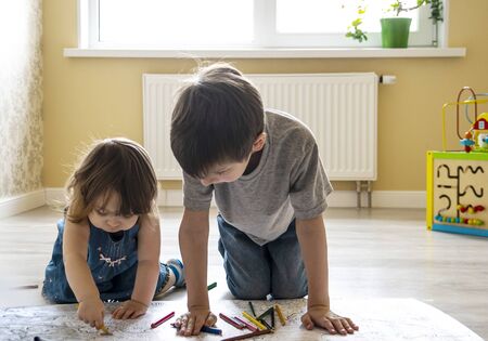 focused children paint a large coloring book on the floor together. quarantine leisure at home conceptの写真素材