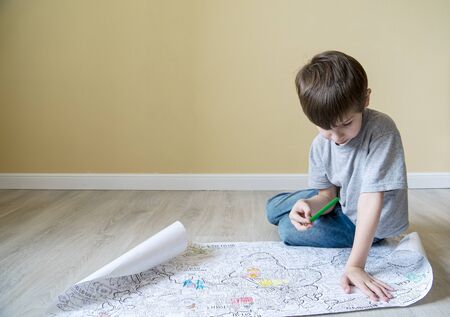 pensive boy examines a large coloring book on the floor with place for text.の写真素材