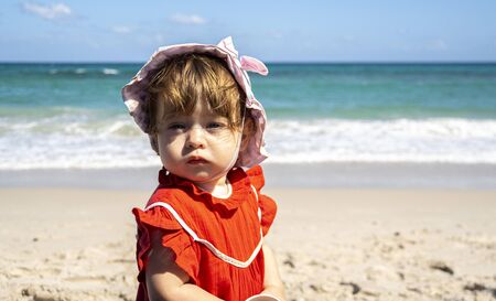 Little cute girl in a red dress looks to the camera thoughtfully.