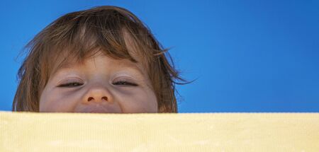 Close-up of a little mischievous and cheerful girl looking out from behind a sunbed.の写真素材