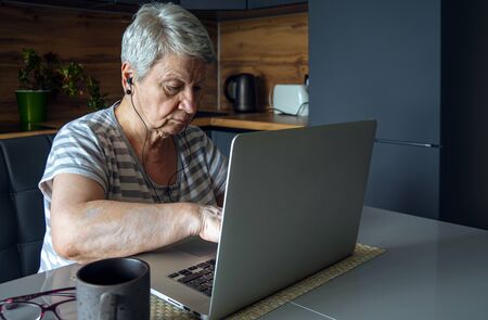 An elderly woman sits at a table and prints on her laptop.