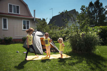 Three pretty preschool girls having fun outside in front of their country house in sunny summer dayの写真素材