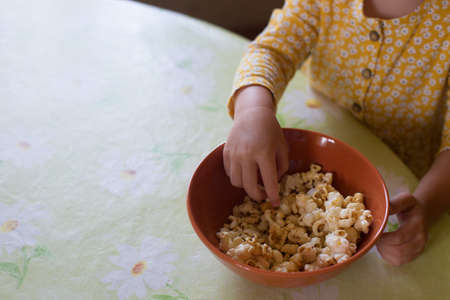 Small girl hands taking popcorn from orange bowlの写真素材