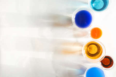 Trendy top view of glasses filled with colotful liquids and their shadows on white background.
