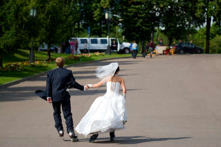 The bride and groom roller skating in the park in sunny summer dayの写真素材
