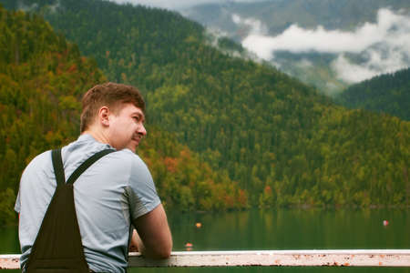 Young man in hiking clothing watching beautiful mountain lake in autumn day. Coniferous forest surround the lakeの写真素材