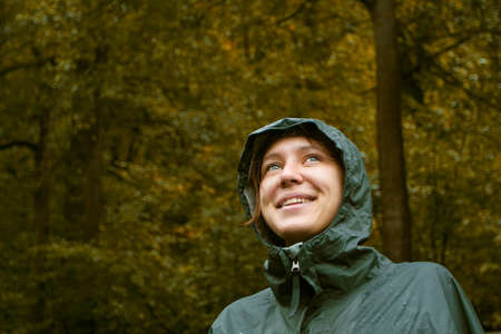 Portrait of happy smiling woman wearing waterproof raincoat with hood in rainy autumn day. Woman is...