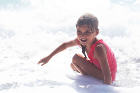 Cheerful preschool girl wearing pink swimsuit having fun in sea wavesの写真素材
