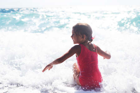 Cheerful preschool girl wearing pink swimsuit having fun in sea wavesの写真素材
