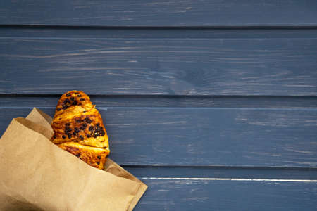 Fresh chocolate croissant in a paper bag lies on a gray wooden background.