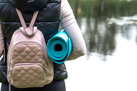 Young woman with backpack and yoga mat standing on the lake.