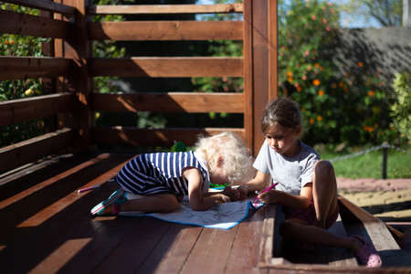 Two girls drawing on wooden veranda in the country house in sunny summer day. Cottagecore aesthetics concept.の写真素材
