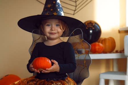 Portrait of a little smiling girl in a witch costume with a pumpkin in her hands.