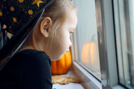 Little cute in Halloween costume and witch hats look out the window.の写真素材