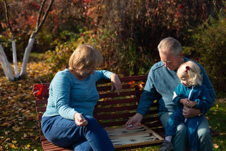 Senior family playing backgammon in their garden in sunny autumn day. Grandfather is keeping his...