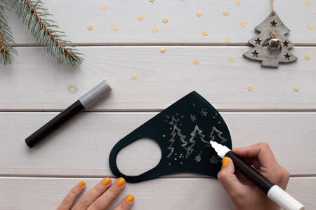 Female hands decorating protective face mask for christmas. New normal new year.