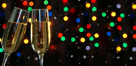 Two champagne glasses on a dark background with a colored garland bokeh