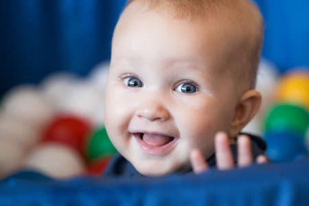 Cheerful smiling baby girl with blond hair and blue eyes sitting in the ball pit. Bright colors portraitの写真素材