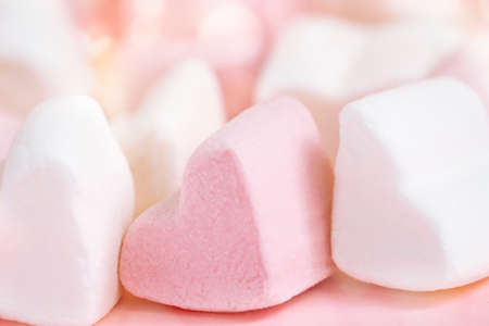 Pink and white marshmallows in the shape of hearts on a pink abstract background with bokeh.