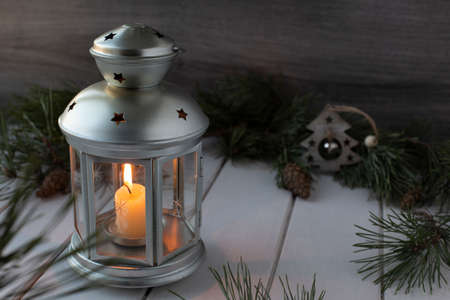 Wax candle in Christmas silver candlestick with stars and spruce branches on white wooden background. New Year decorationの写真素材