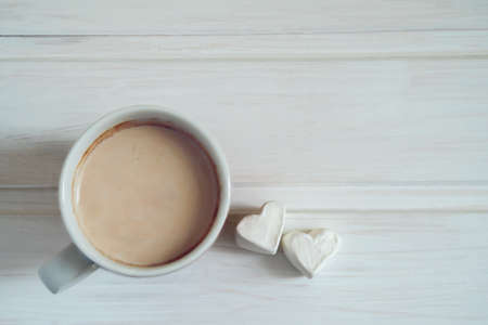 Mug with cocoa and two heart-shaped marshmallows on white wooden background.