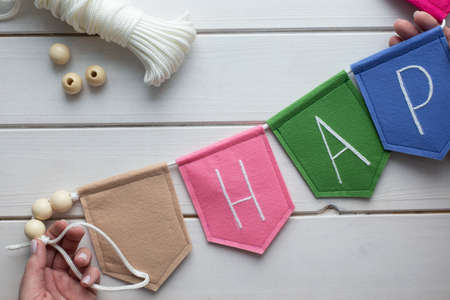 How to make felt flag garland with embroidered letters at home. Step by step instructions. Hands making DIY project. Step 8: create garland from flags using rope. Don't forget to make loop for bindingの写真素材