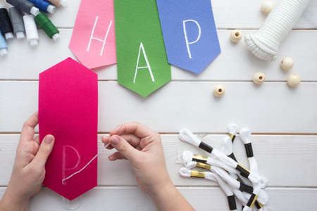 How to make felt flag garland with embroidered letters at home. Step by step instructions. Hands making DIY project. Step 6: embroider letters on felt using outline stich or your favorite oneの写真素材