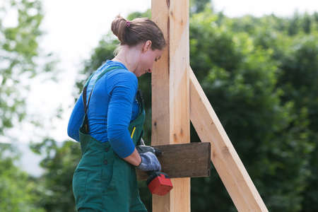 Young woman working with screw driver. Woman is constructing outdoors in summer day. Diversity and...