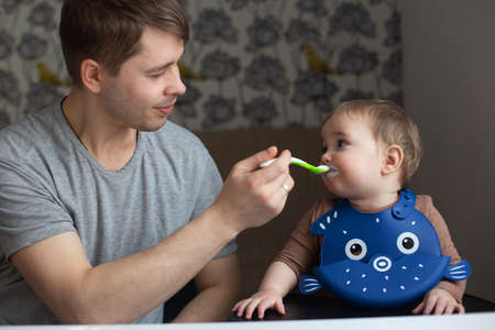 Young father feeding his baby in the kitchen. Family time and gender equality concept. Lifestyleの写真素材