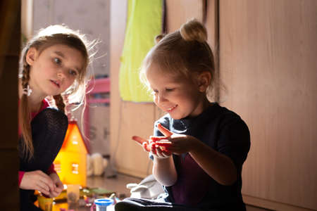 Two girls playing together in morning sun light sitting on the floor. Carefree childhood concept. Indoorsの写真素材