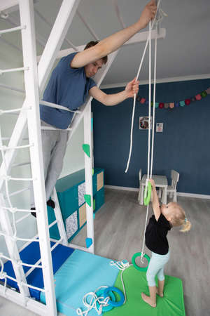Young father and his small blond daughter constructing home sports complex. Family is hanging rings. Home improvement and fathers day concept. Kids room interiorの写真素材