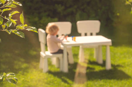 Summer background with unfocused image of little girl playing at a table.の写真素材
