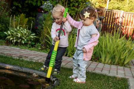 Two girls pumping water with childrens pumps from a small pond.の写真素材