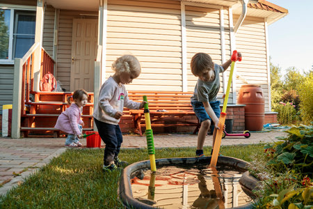 Children playing in the garden with water pump near a small pond.の写真素材