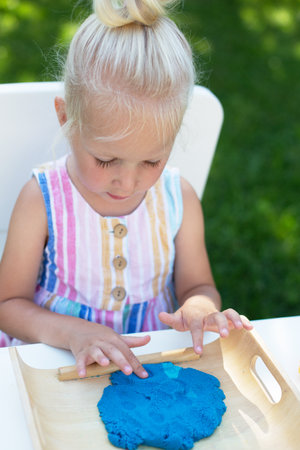 Little cute girl with blonde hair playing with colorful kinetic sand outdoors in the backyard in summer day. Hobby, leisure activity, crafting, modeling and creative hobby conceptの写真素材
