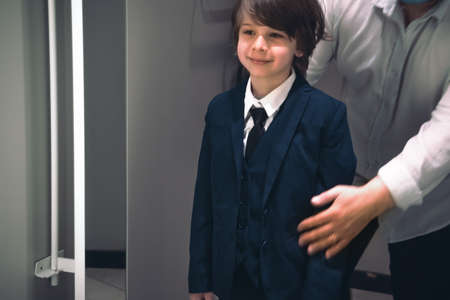 Smiling boy and his father trying school uniform for future schooler.