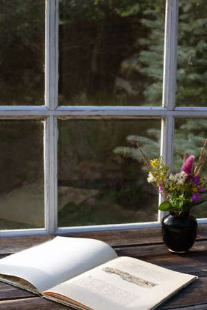 Rustic retro atmosphere with old book and bouquet of wild flowers on wooden table at the terrace. Vertical format, copy spaceの写真素材