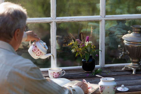 Senior man reading drinking tea terrace summer. Rustic old windowの写真素材