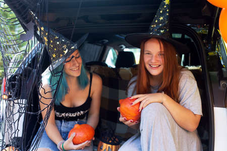 Two girls generation Z celebrating Halloween car trunk. Autumn holidays