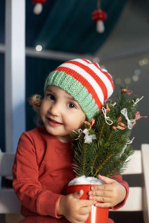 Cheerful little girl Santa hat holding small Christmas tree handsの写真素材