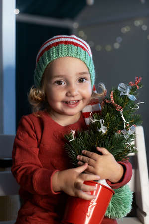 Cheerful little girl Santa hat holding small Christmas tree handsの写真素材