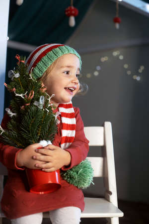 Cheerful little girl Santa hat holding small Christmas tree handsの写真素材