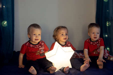 Triplets sitting on the bed decorated for Christmas. Three cute little kids in red t-shirtsの写真素材