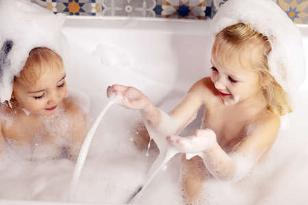 Two kids little girls sisters having fun in bathroom playing with bath foam. Kids personal care