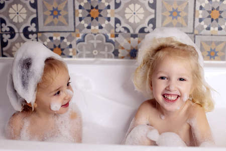 Two kids little girls sisters having fun in bathroom playing with bath foam. Kids personal care