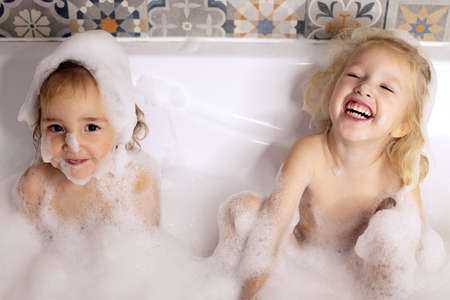 Two kids little girls sisters having fun in bathroom playing with bath foam. Kids personal careの写真素材