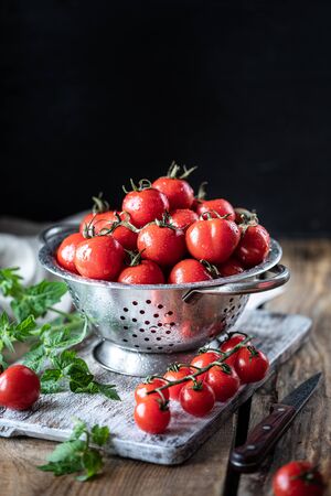 Group of red cherry tomatoes in a metal colander on a wooden table.の写真素材